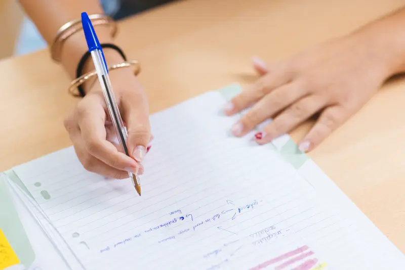 Gros plan sur les mains d'une élève annotant un cahier de cours